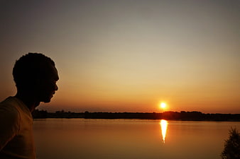 Silhouette of Man Watching Sunset Over Calm Lake