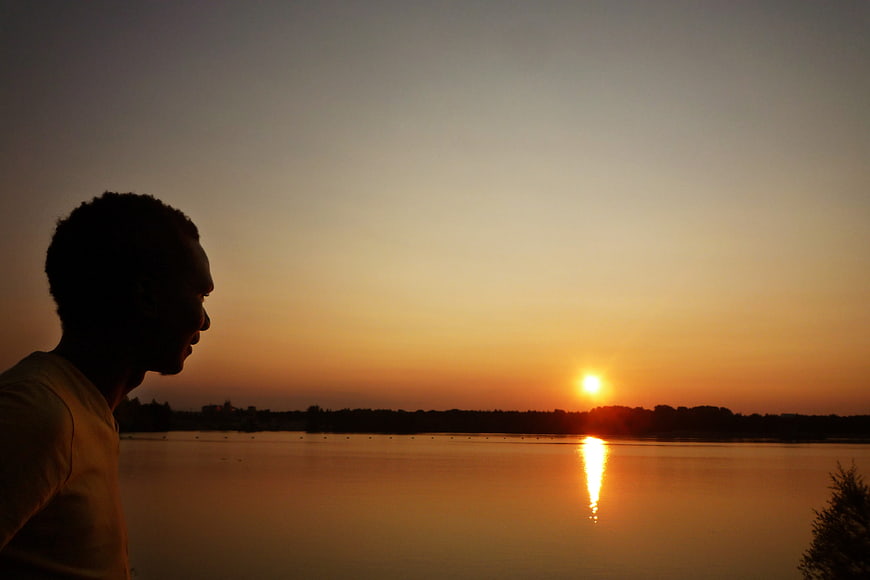 Silhouette of Man Watching Sunset Over Calm Lake