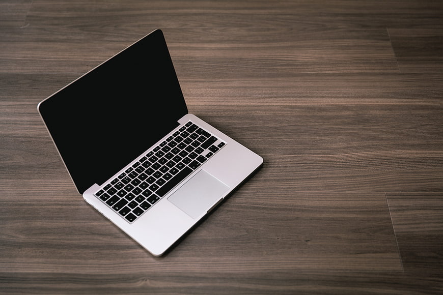 Open silver laptop with black screen on dark wooden floor