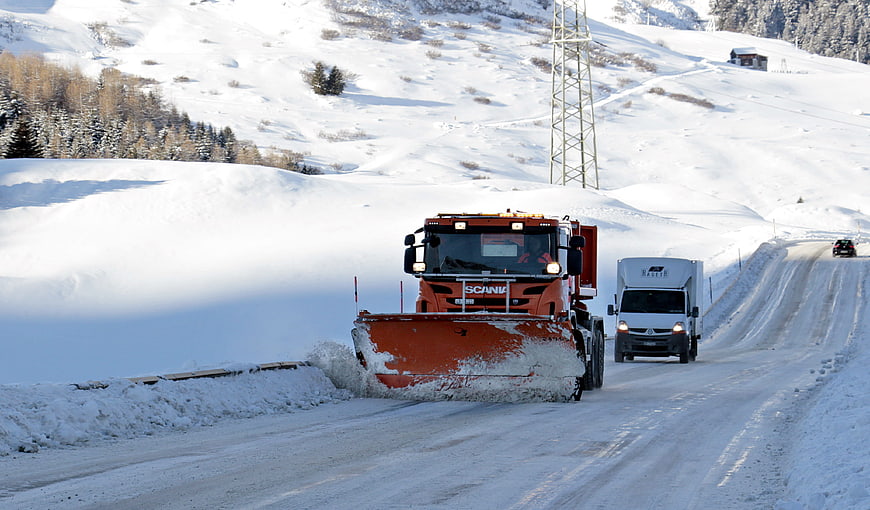 Orange snowplow clearing mountain road in winter