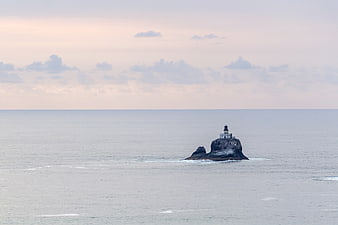 Lighthouse on Rocky Island in Calm Ocean at Dusk
