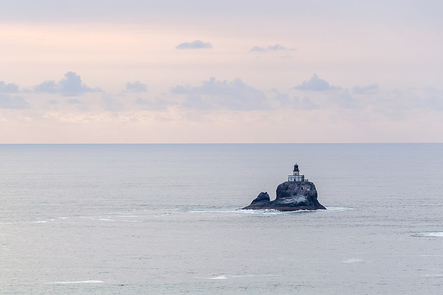 Lighthouse on Rocky Island in Calm Ocean at Dusk