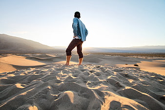 Man standing on sand dune looking at desert sunset