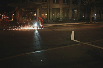 Worker grinding sparks on city street at night