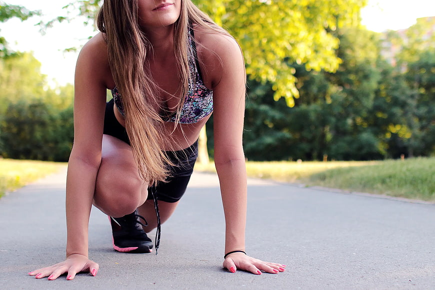 Woman in athletic wear crouching on paved path outdoors