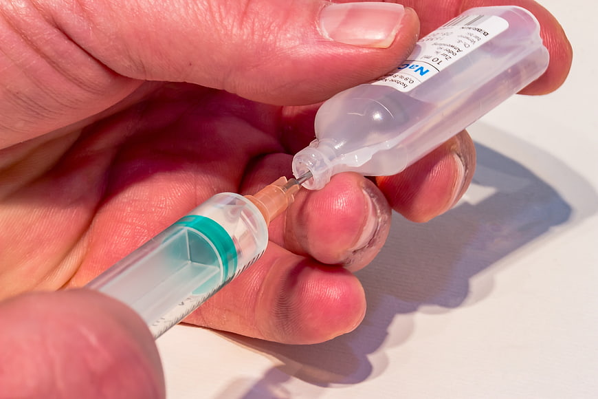 Close-up of hands drawing saline solution from a vial into a syringe