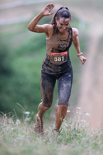 Muddy female runner in action during obstacle course race