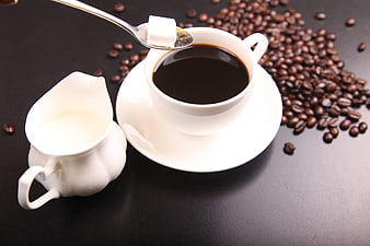 Black coffee cup with sugar cube, milk jug, and coffee beans
