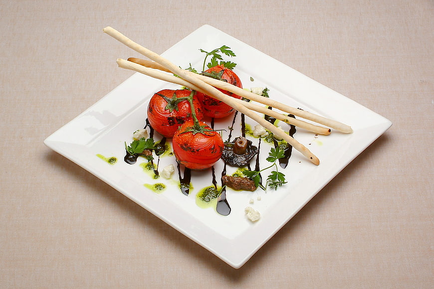 Gourmet roasted tomatoes with breadsticks on white plate