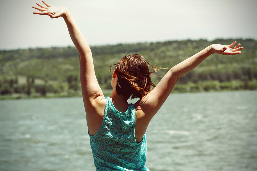 Woman with arms raised by lake enjoying freedom