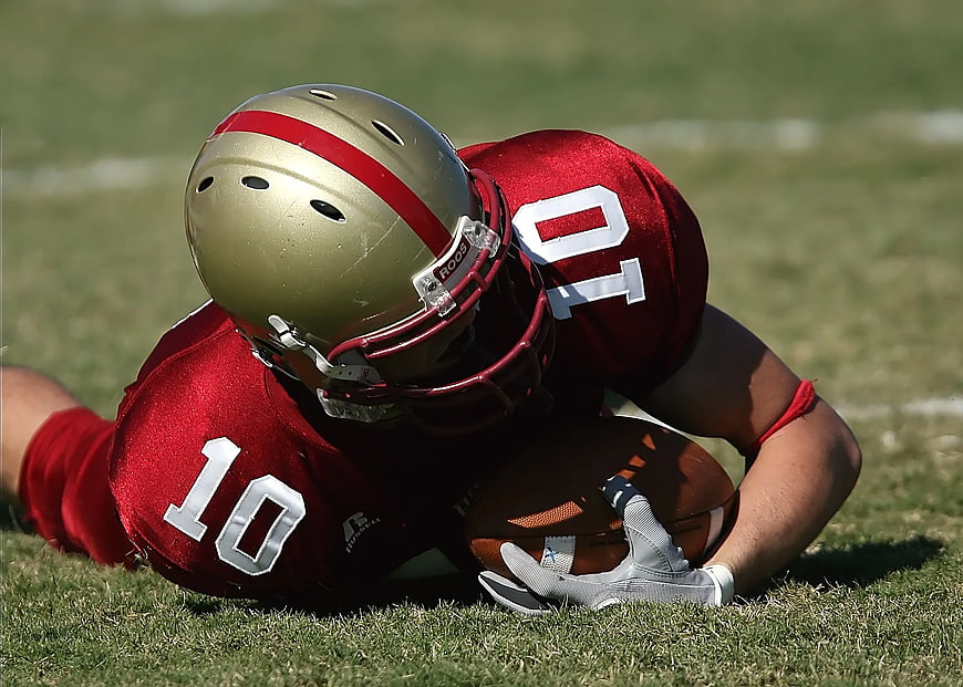 American Football Players Tackling on Grass Field