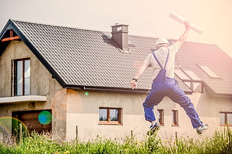 Builder jumping with blueprints in front of new house