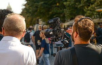 Filmmaker filming crowd with camera and microphone outdoors
