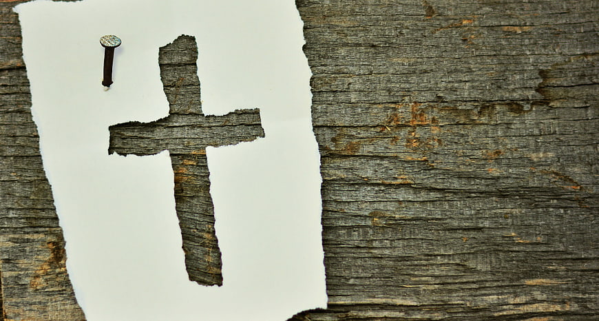 Rustic wooden cross cutout on white paper with nail