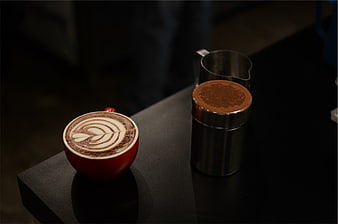 Red Latte with Art and Cocoa Shaker on Dark Table