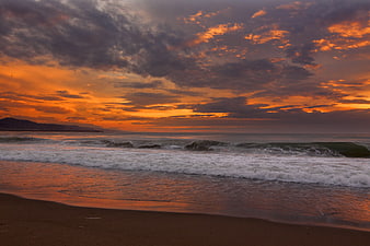 Dramatic Orange Sunset Over Ocean Waves and Sandy Beach