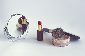 Red lipstick, makeup brush, and powder on white background