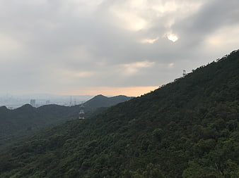 Lush green mountain ridge with city skyline and power lines