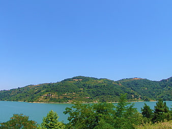Serene Lake Surrounded by Green Hills and Blue Sky