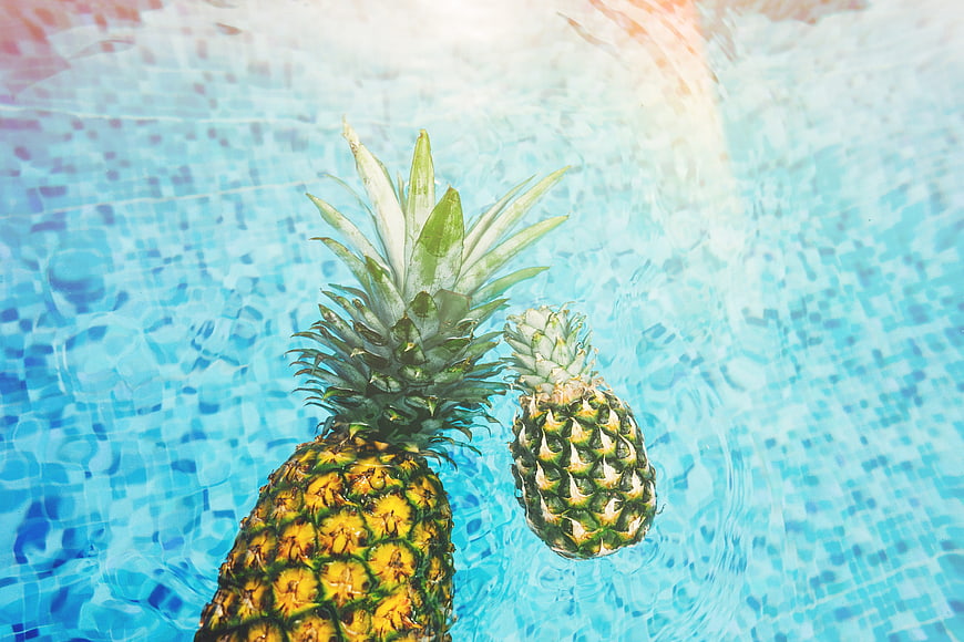 Two pineapples floating in a blue swimming pool