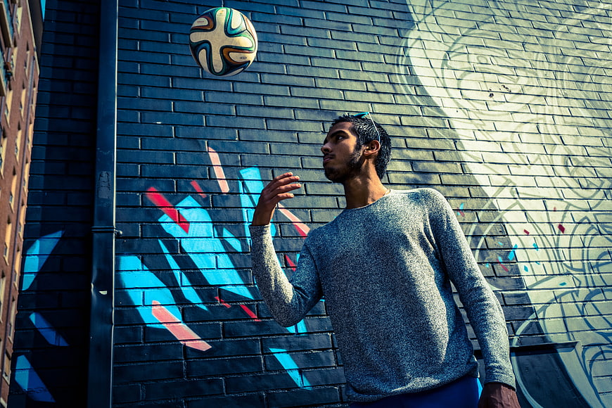 Young man juggling soccer ball against graffiti wall