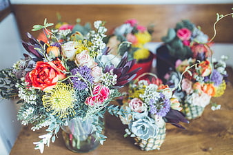 Colorful floral arrangements in glass and pineapple vases on wood