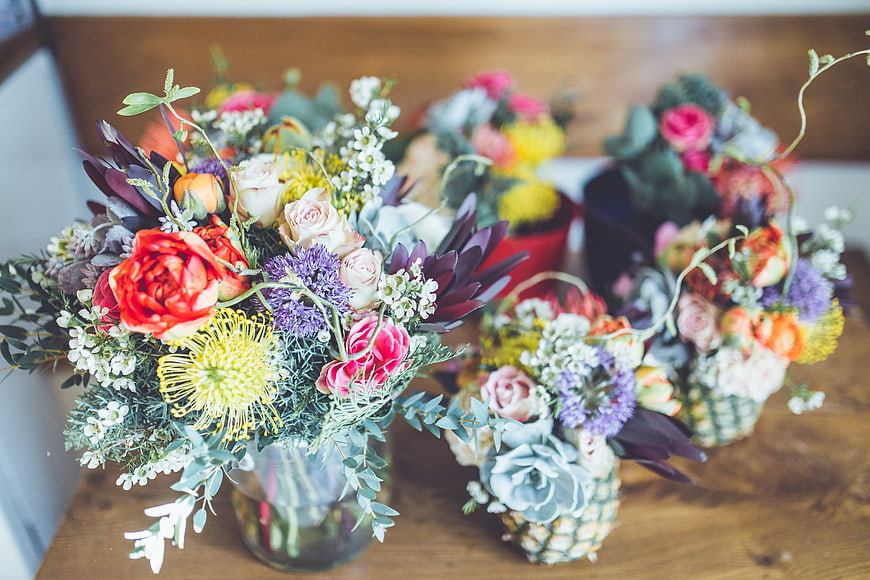 Colorful floral arrangements in glass and pineapple vases on wood