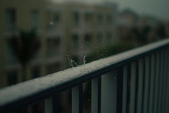 Raindrops splashing on a balcony railing with blurred city background