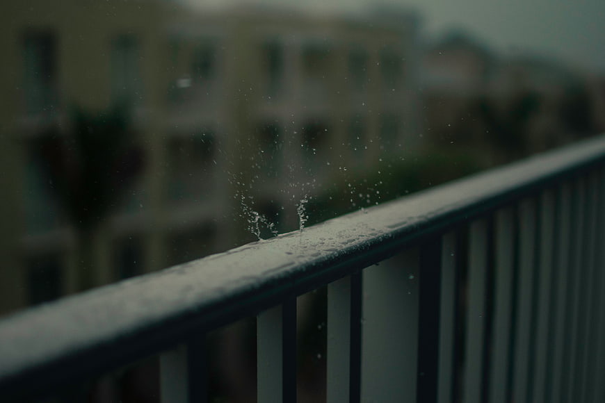 Raindrops splashing on a balcony railing with blurred city background