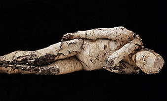 Reclining wooden sculpture of a man on black background