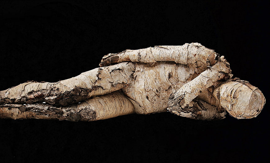 Reclining wooden sculpture of a man on black background