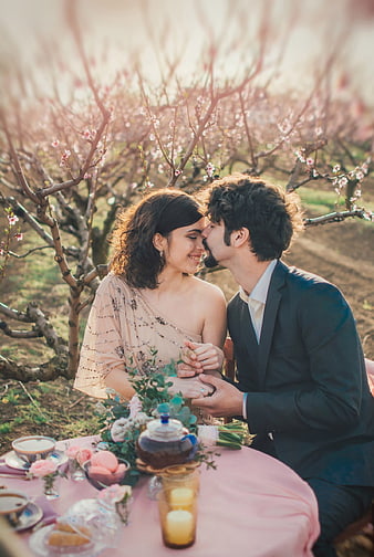 Romantic couple sharing a kiss at a tea table in a blooming orchard