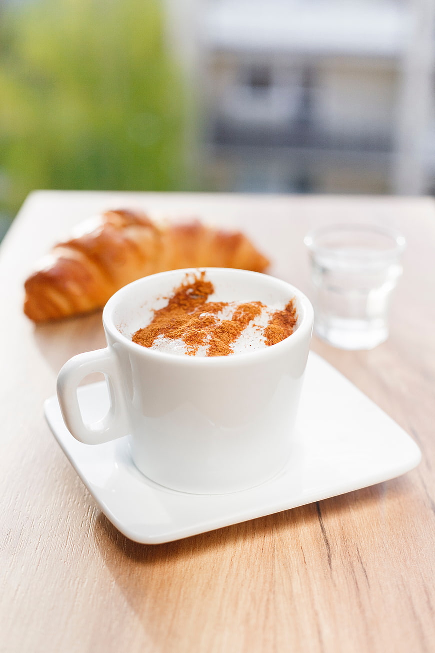Cappuccino with cinnamon and croissant on wooden table