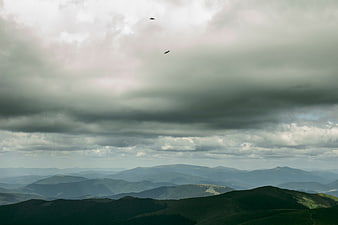Dramatic mountain landscape with birds flying under storm clouds
