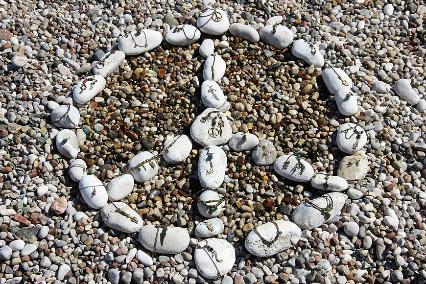 Peace sign made of white stones and jewelry on pebble beach