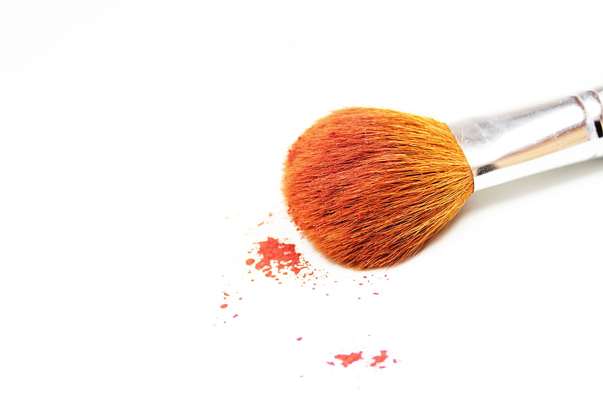 Orange makeup brush with red powder on white background