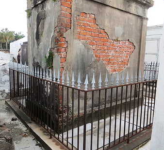 Weathered brick mausoleum with iron fence in New Orleans cemetery