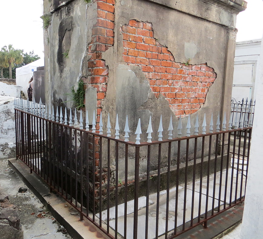 Weathered brick mausoleum with iron fence in New Orleans cemetery
