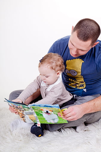 Father Reading Book to Toddler Daughter on White Rug