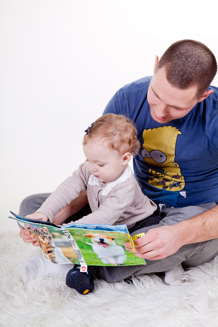 Father Reading Book to Toddler Daughter on White Rug