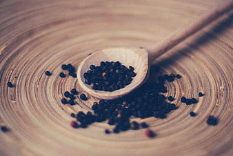 Black peppercorns in wooden spoon on rustic board