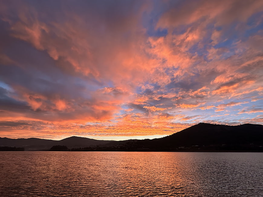 Vibrant Orange Sunset Over Lake with Silhouetted Mountains