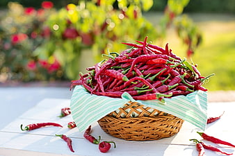 Fresh red chili peppers in a wicker basket on a white table