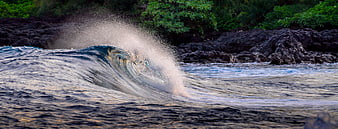 Powerful ocean wave crashing against dark volcanic rocks