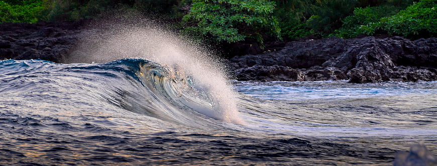 Powerful ocean wave crashing against dark volcanic rocks