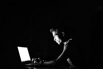 Man typing on laptop in dark room black and white