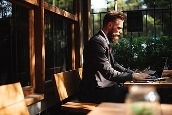 Bearded businessman in suit working on laptop at outdoor cafe table