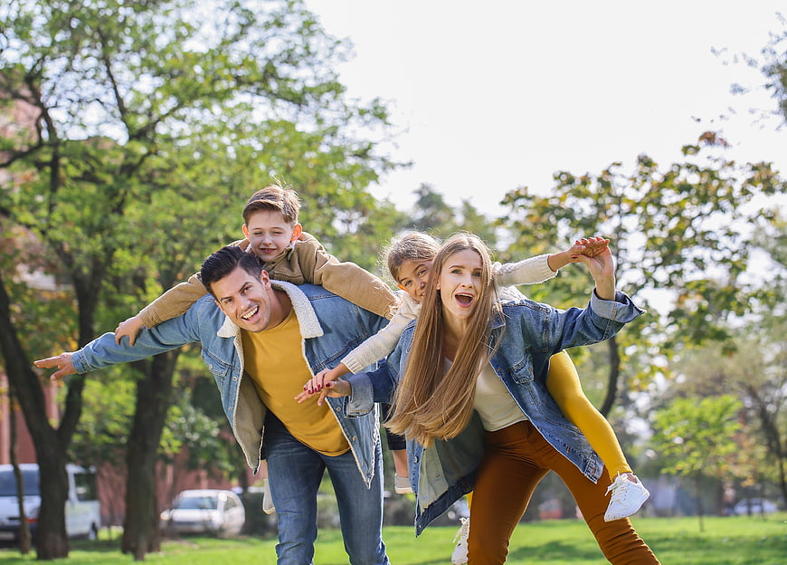 Happy family playing piggyback in sunny park