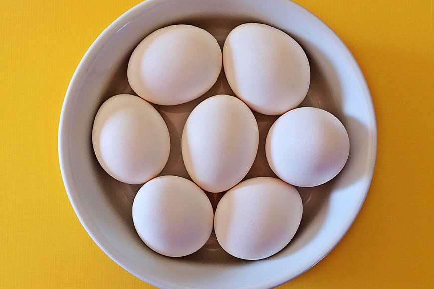 Top View of White Eggs in White Bowl on Yellow Background