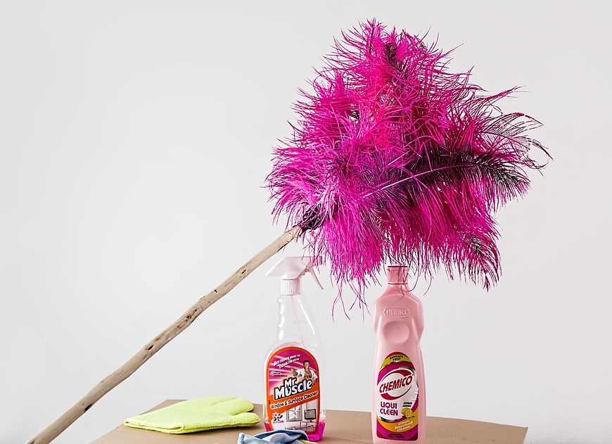 Pink Feather Duster and Cleaning Supplies on Wooden Surface